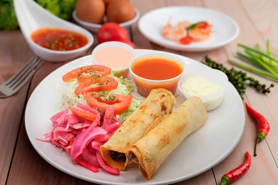 Plate with salad, burritos and three sauces on the side