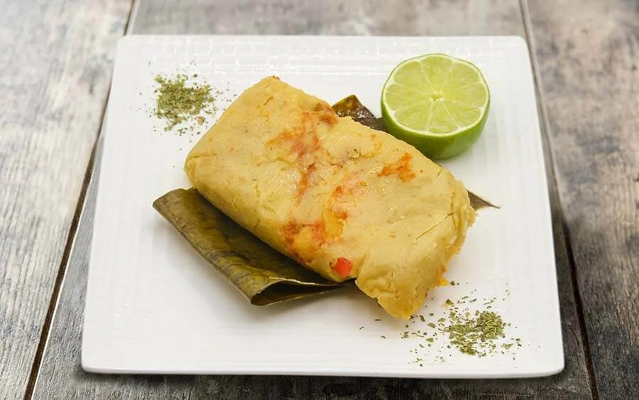 White plate on a brown table with a tamale and a lemon on the side 