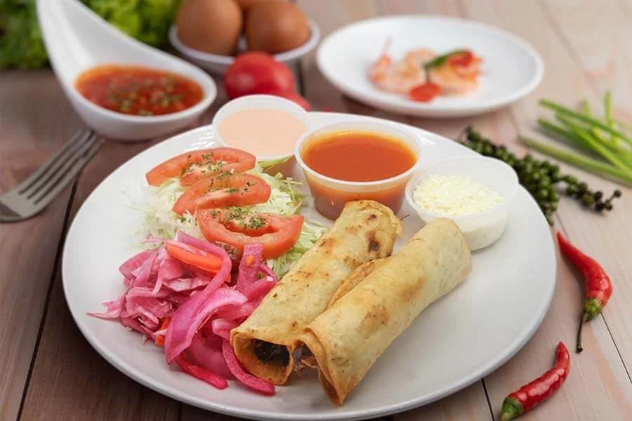 Plate with salad, burritos and three sauces on the side 