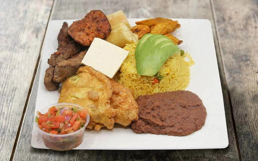 Plate of yellow rice with avocado on top, meat, beans, salad, cassava and sweet plantains 